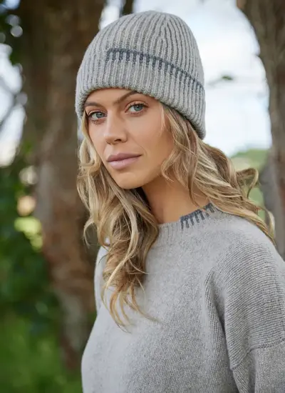 Woman wearing a ribbed wool cashmere beanie by Fisherman Out of Ireland with contrast blanket stitch detail in grey tones.